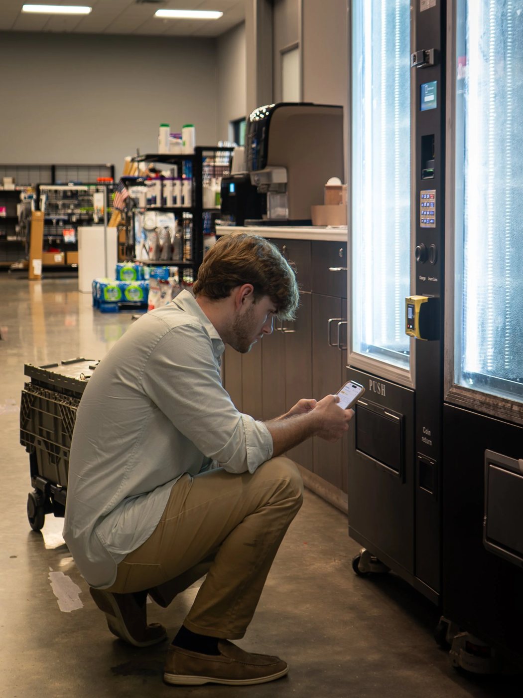 A man kneeling beside a vending machine checking his phone.